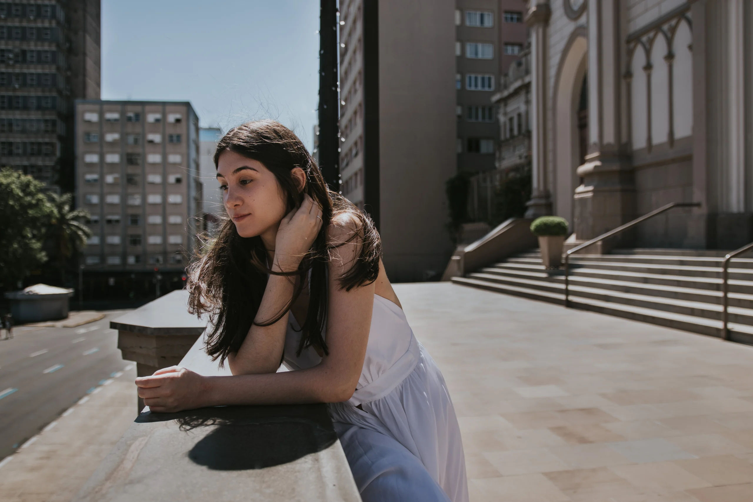 Mariana escorada na balaustrada em frente à Catedral, contemplativa.