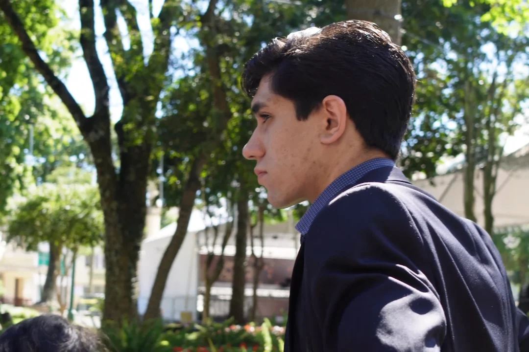 O autor, de perfil, com olhar sério e observador, junto de árvores de uma praça.