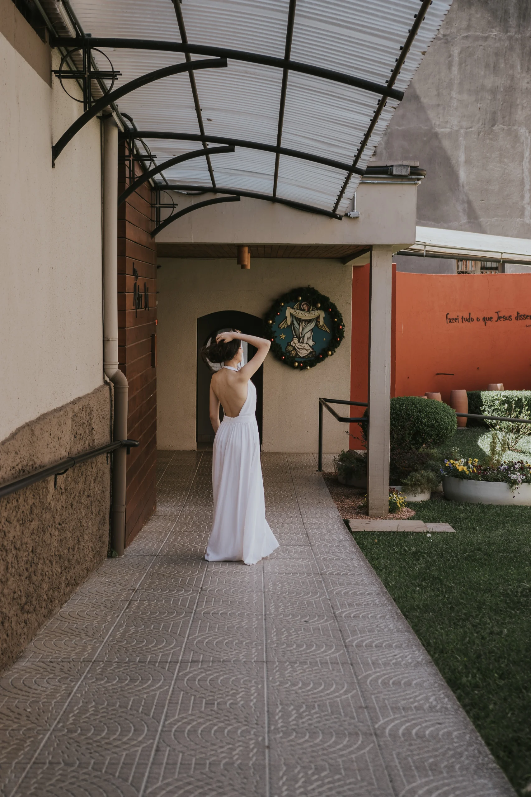 Mariana, distante, de costas, uma mão sobre o cabelo.