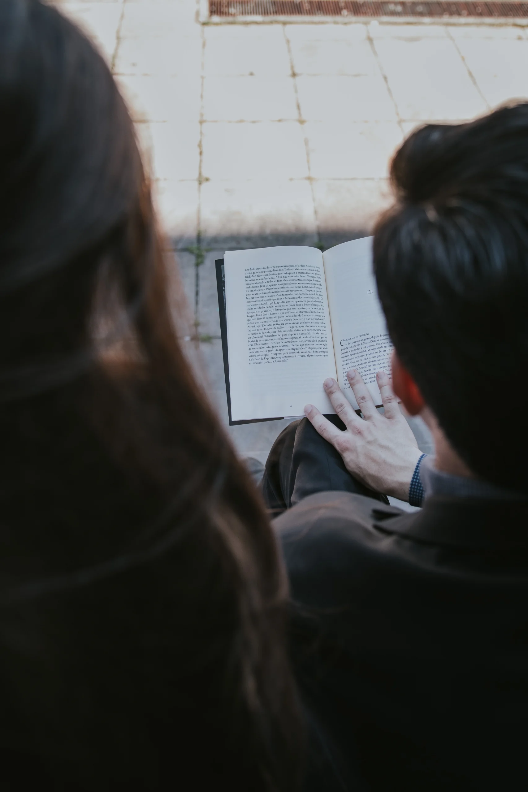 O autor e Mariana, de costas, diante das páginas do livro que estão a ler.